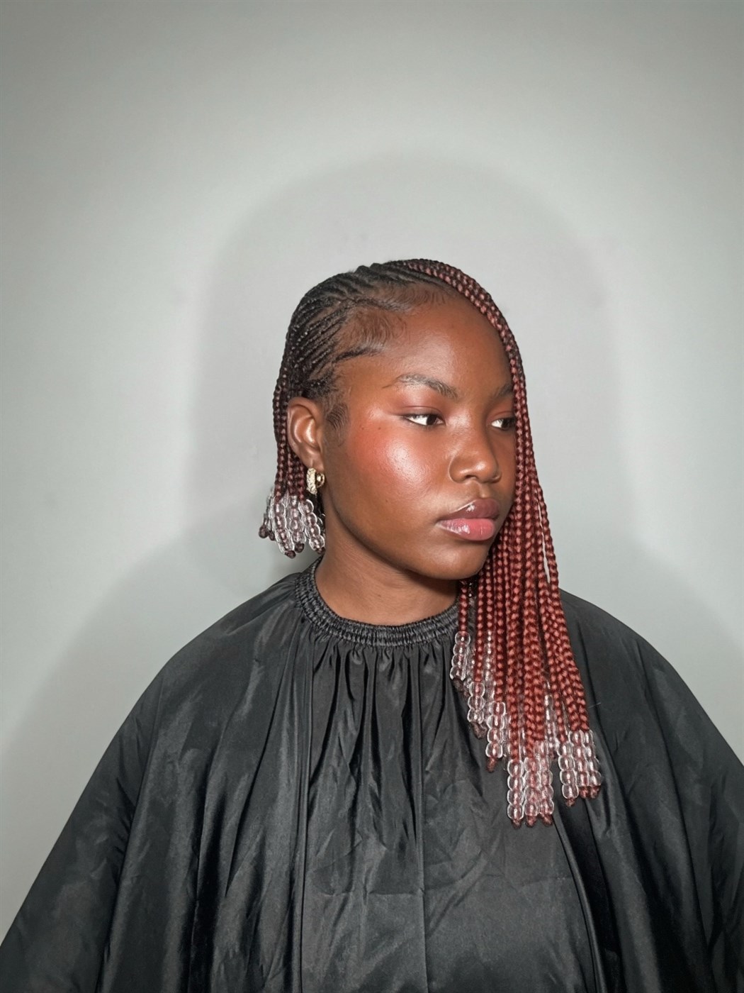 A client in the lounge wearing auburn braids with clear beaded ends, cornrowed close at the sides
